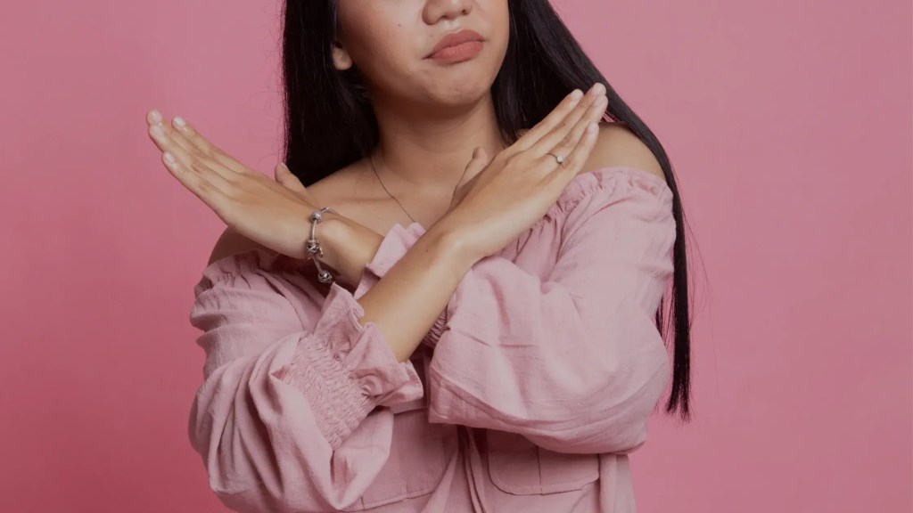 Une femme aux cheveux bruns qui croise les bras et les mains en X pour mentionner le refus. On ne voit pas le haut du visage seulement le bas du visage jusqu'au coude.